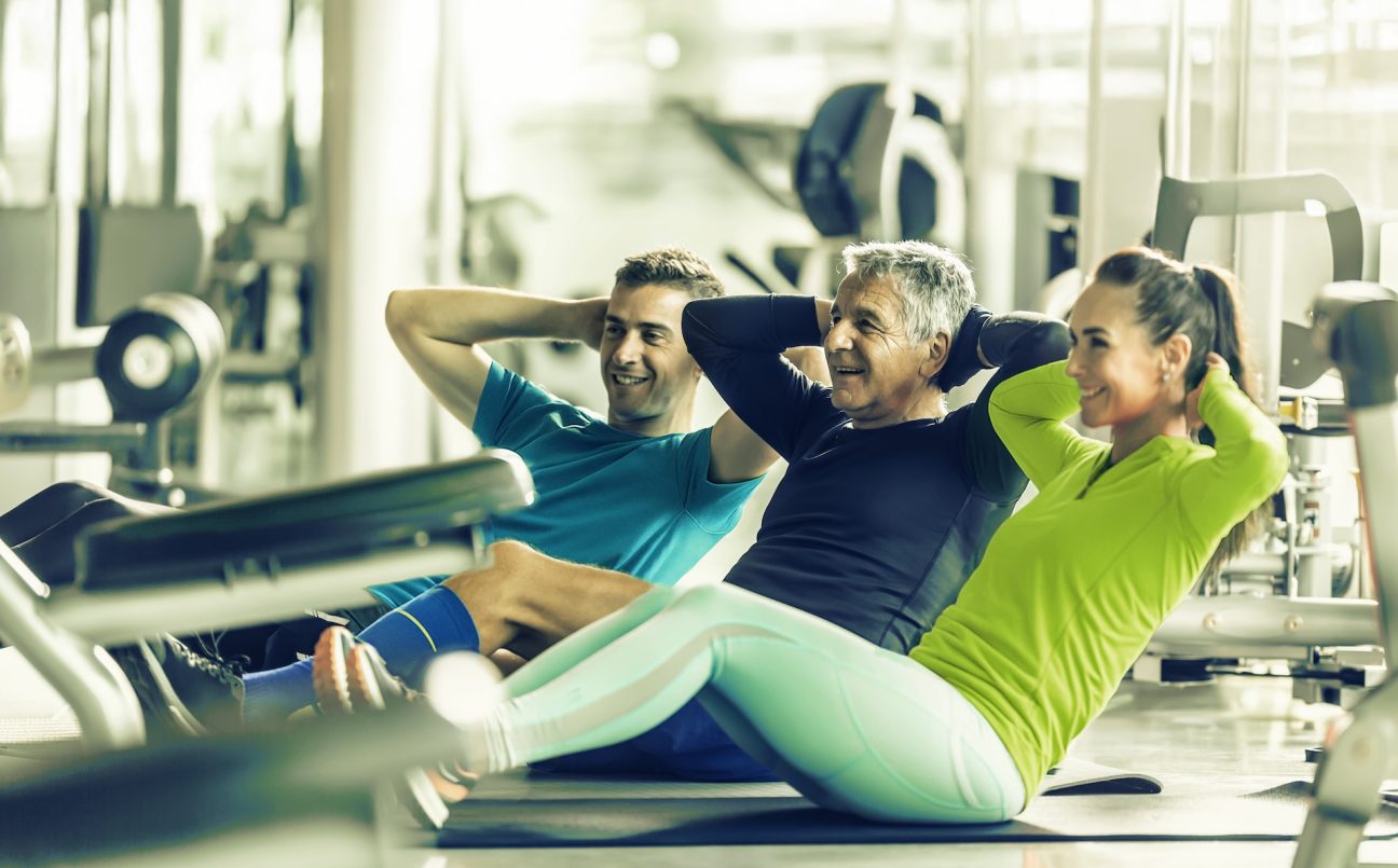 A woman and two men in the gym doing situps to gain physical and mental health benefits.